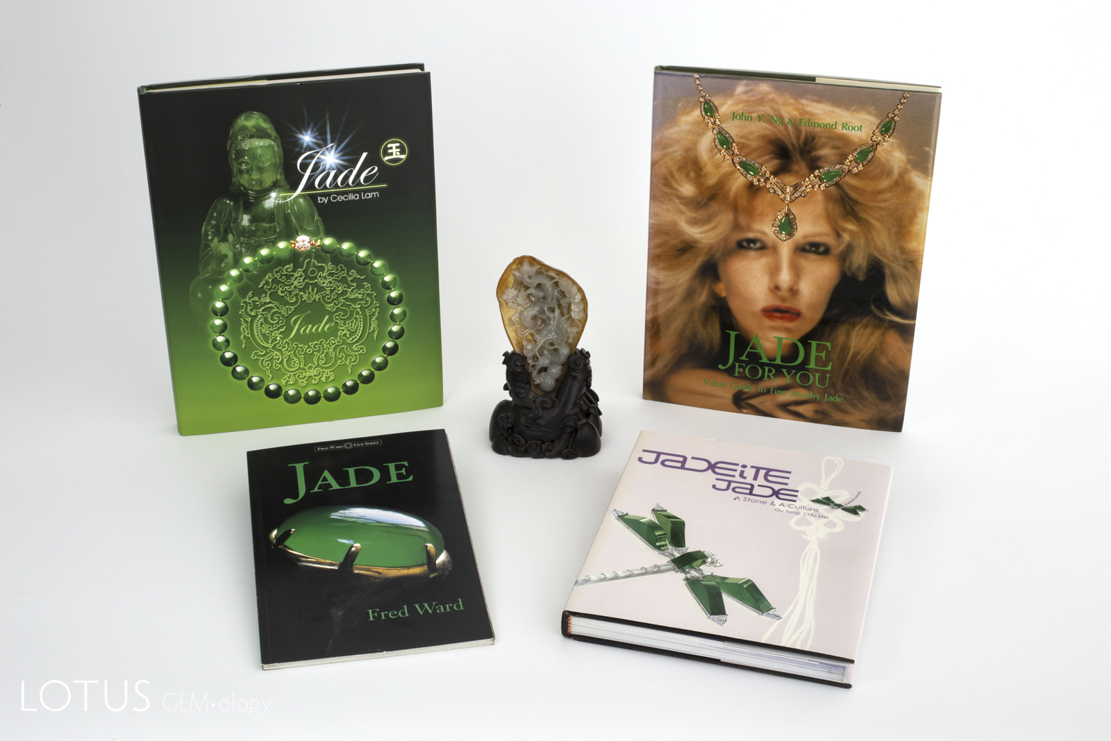 Four classic modern books on jade surround a Chinese carving in Burmese jade. Clockwise from top left: Jade by Cecilia Lam; Jade for You by John Ng & Edmond Root; Jade by Fred Ward, and Jadeite Jade: A Stone & a Culture by Ou Yang Chiu Mei.