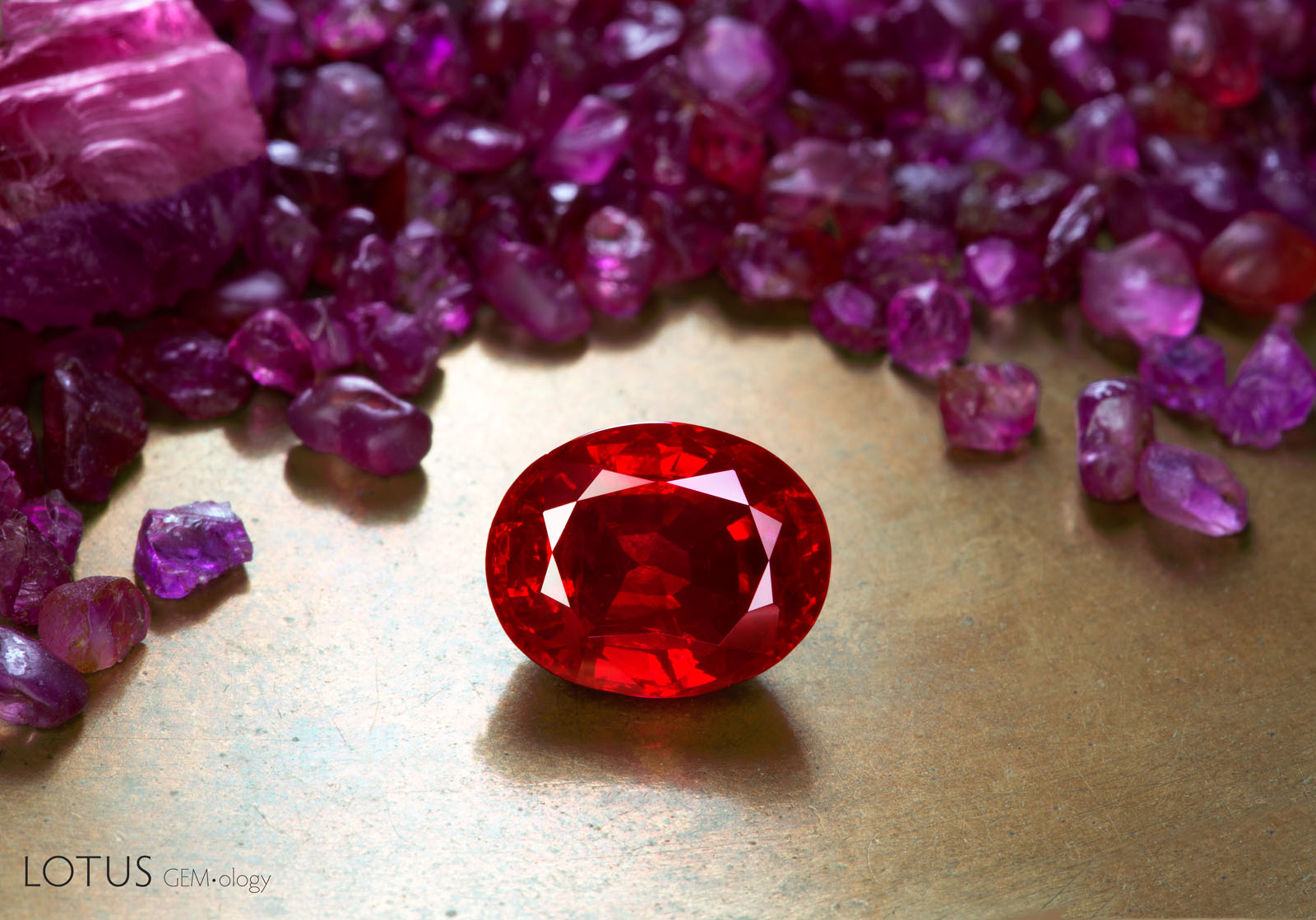 Figure 1. A faceted heated ruby from Mogok, Myanmar, weighing more than 3 ct, stands out against a backdrop of untreated ruby rough from the same origin. The striking appearance of Mogok ruby is highly sought after. Photo by Wimon Manorotkul; faceted ruby courtesy of Kiarttichatra Intarungsee.