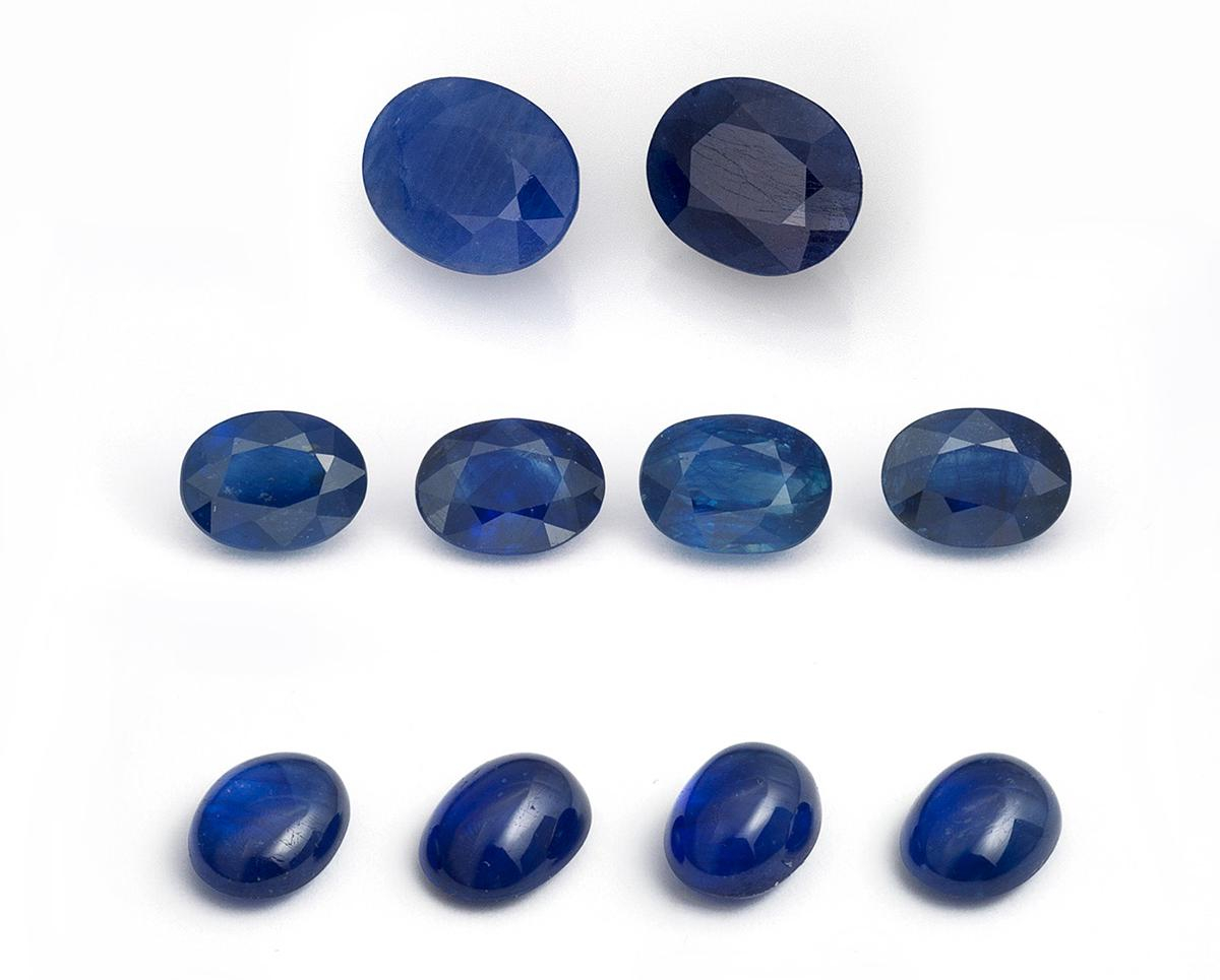 Figure 2. Two first-generation cobalt-doped glass-filled sapphires (top row; 3.49 & 3.37 ct), along with eight latest-generation cobalt-doped glass-filled sapphires ranging from 1.50–2.25 ct each that were tested as part of this study. Note the far lower clarity of the first-generation stones. Photo: Wimon Manorotkul