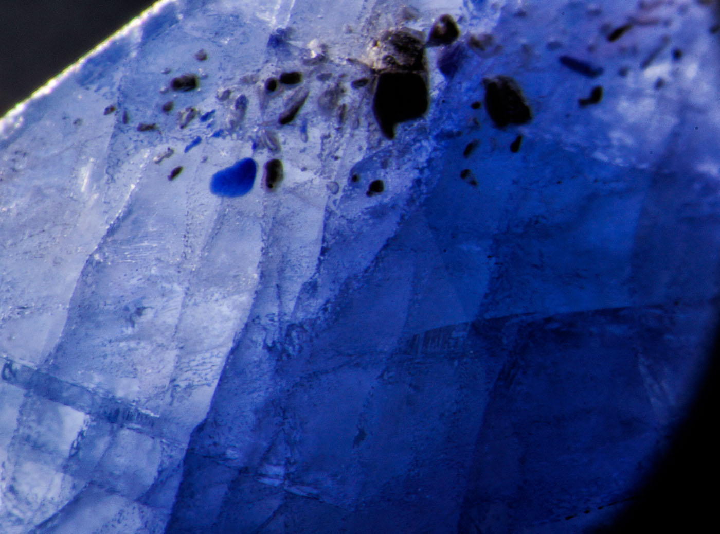Figure 5. Left: Blue pool of cobalt-doped glass fills a surface cavity in this first-generation Tanusorn stone. Dark-field illumination. Right: The same inclusion in reflected light reveals the lower luster of the glass filler. Oblique fiber-optic illumination. (Photos: Richard Hughes). Lotus Gemology.