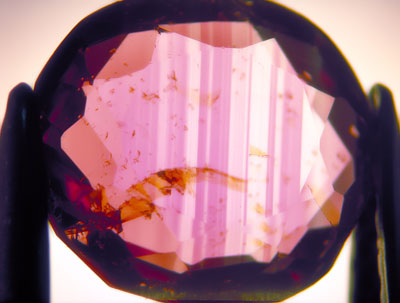 This Burmese ruby is cut so shallow that light passes straight through, revealing strong color zoning and yellow stains in feathers. In this stone, brilliance is almost entirely absent, with only a large central window and extinction near the edges being visible. Photo by the author.
