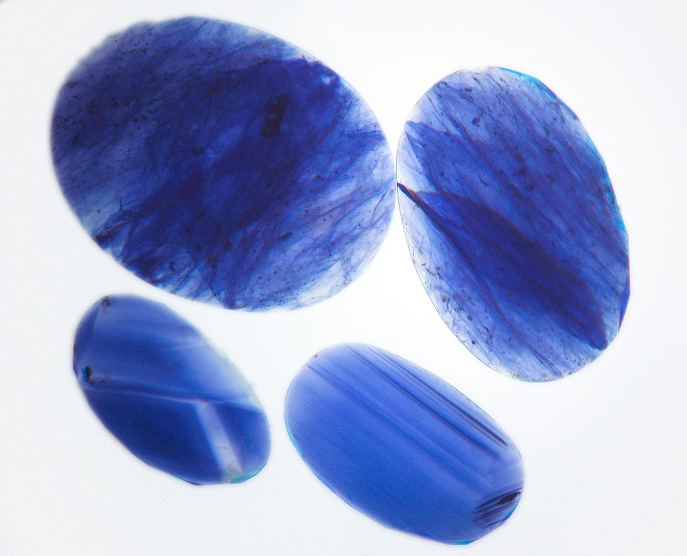 Figure 12. Immersion in di-iodomethane (methylene iodide) in diffuse light-field illumination quickly reveals the blue color concentrations in the cobalt-glass filled sapphires (top two stones), whereas natural sapphires show angular color zoning (lower two stones). Image corrected to remove yellow color of liquid. Photo: Wimon Manorotkul