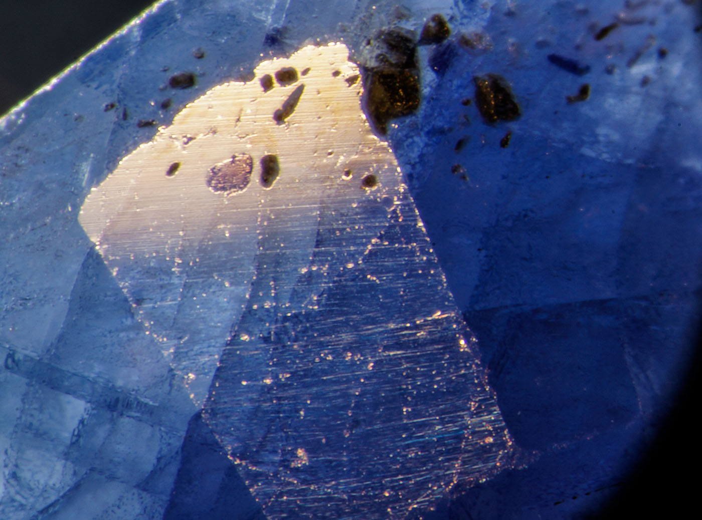 Figure 5. Left: Blue pool of cobalt-doped glass fills a surface cavity in this first-generation Tanusorn stone. Dark-field illumination. Right: The same inclusion in reflected light reveals the lower luster of the glass filler. Oblique fiber-optic illumination. Photos: Richard Hughes
