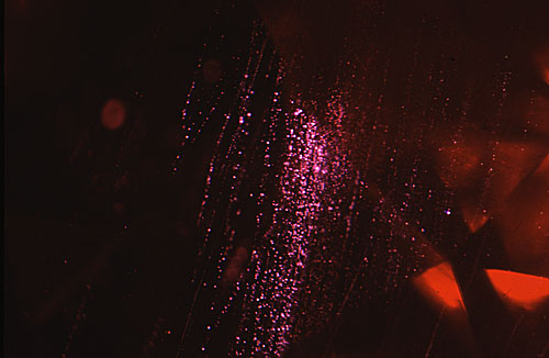 Figure 4. Fiber-optic illumination reveals the rain-like stringers of flux particles in the Kashan ruby that are so typical of this type of synthetic. Magnified 15×. Photomicrograph © John I. Koivula, microWorld of Gems.