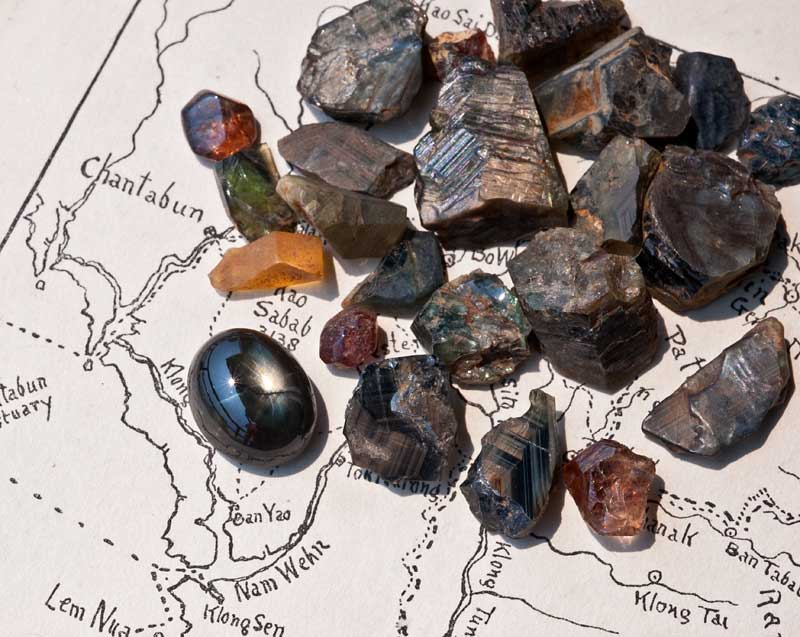 Rough gems from Khao Ploi Waen, along with one 12-rayed black star sapphire cabochon. The deep red stones are zircon; the rest are sapphire. Photo © Wimon Manorotkul.