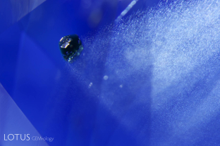 An unusual green crystal was found trapped in this unheated blue sapphire from Serendib, with a cloud of rutile silk trailing in its wake.