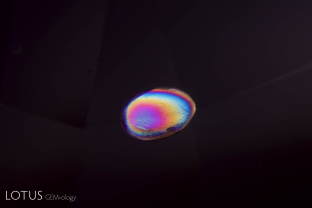 A transparent birefringent crystal cut through on the surface of this natural spinel from Mogok stands out in high contrast when viewed between crossed polars.