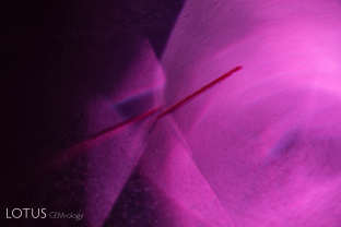 Growth tube with epigenetic iron-oxide staining in an untreated ruby from Mozambique. Positioned along the rhombohedron edge, this superficially resembles a boehmite needle, but there is no associated twinning.