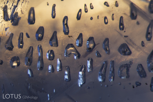 Clustered negative crystals like these grew syngenetically, meaning at the same time as their sapphire host. Note their angular “euhedral” shapes. Many contain black flakes of graphite.