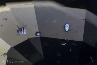 Feldspar crystals are a frequent guest of sapphires derived from basalt deposits. Thus it was no surprise when the three larger crystals show here turned out to be feldspar. The identification was made with Lotus Gemology’s micro Raman unit. Examination with crossed polars reveals the doubly refractive nature of the feldspar guest inclusions.