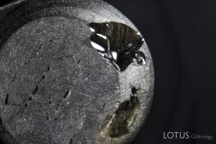 This black star sapphire had large pits on the base filled with dopping varnish. Following removal of the varnish by soaking in alcohol, the 75-ct stone lost about 0.25 ct of weight. But careful examination after the varnish removal revealed something far more sinister, a layer of glass coating the inside of the cavities. Note the perfectly smooth curved cavity surfaces, nothing like what one would expect for the broken surface of sapphire. In addition, we could see the the glass extended across much of the base.