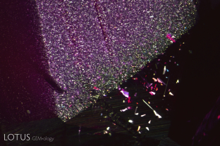 During a crystal’s growth, conditions may change. The result is reflected by growth features such as zoning, twinning, dislocations, etc. These changes may also influence events that occur after the growth, such as exsolution (the unmixing of a solid solution). In this Mozambique ruby, we can see a zoned cloud of fine exsolved particles that shifts dramatically to much larger exsolved needles/plates.