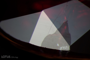 Both the cavity and its associated fissures on the edge of this ruby display a lower luster than the surrounding corundum, providing evidence that the stone has been glass filled.