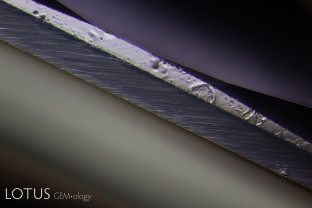 The high temperature that this blue sapphire from Madagascar was exposed to during beryllium diffusion treatment melted part of the girdle of the stone. Also, in the lower right corner of the photo is the tiny ablation spot that the LIBS created in order to detect the beryllium.