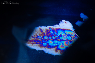 High temperature heat treatment has created irregular, iridescent thin film patterns in this blue sapphire. In the background, clouds of dotted, partially dissolved silk can be observed.