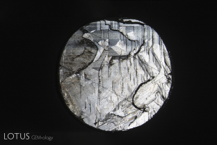 Basal parting seen on the back of a black star sapphire from Chanthaburi, Thailand. Note the step-like appearance. The two diagonal lines are rhombohedral parting planes. Basal parting in these stones is due to exsolution of hematite/ilmenite silk, which produces both the star effect and a lack adhesion.