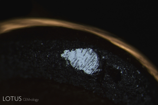 A small rhombohedral parting plane on the girdle of a black star sapphire from Chanthaburi, Thailand. This parting is cause by exsolution of boehmite, which produces a lack of adhesion.