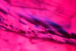 In the foreground you can see flattened gas bubbles in a fissure, while in the background you can see blue flashes of color, both indicators that this ruby is lead glass filled.