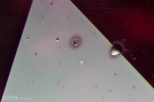 The shiny, droplet-like marks on the surface may look like water or oil, but they are actually spall marks. They do not rub or scrape off, but are fused onto the surface as a result of heat treatment. This example is on a heated Madagascar pink sapphire.