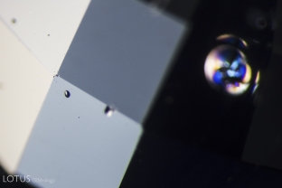 In the foreground on the left, a spall mark is visible, providing a piece of evidence that this stone was heated. Although it looks like a small water droplet, it is “frozen” in place and cannot be rubbed or scraped off. In the background, we also see a shiny melted crystal “discoid,” confirming that the stone is heated.