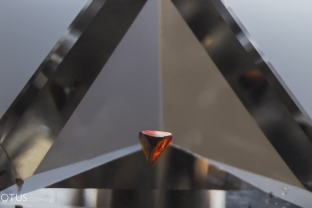 A reddish orange sphalerite crystals hangs suspended in quartz.