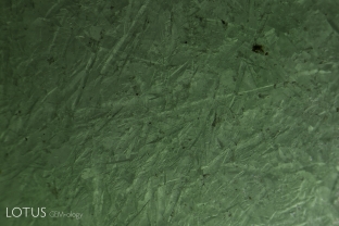 In this devitrified glass imitation of jadeite jade, high magnification reveals random arrangements of tiny crystals where the glass has begun to crystallize.